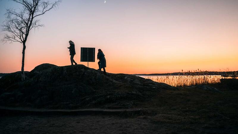 Två kvinnor går längs en klippa i solnedgången, hukade över sina mobiltelfoner. Det är något oroligt över bilden. Kanske försöker de kontakta någon som är försvunnen. 