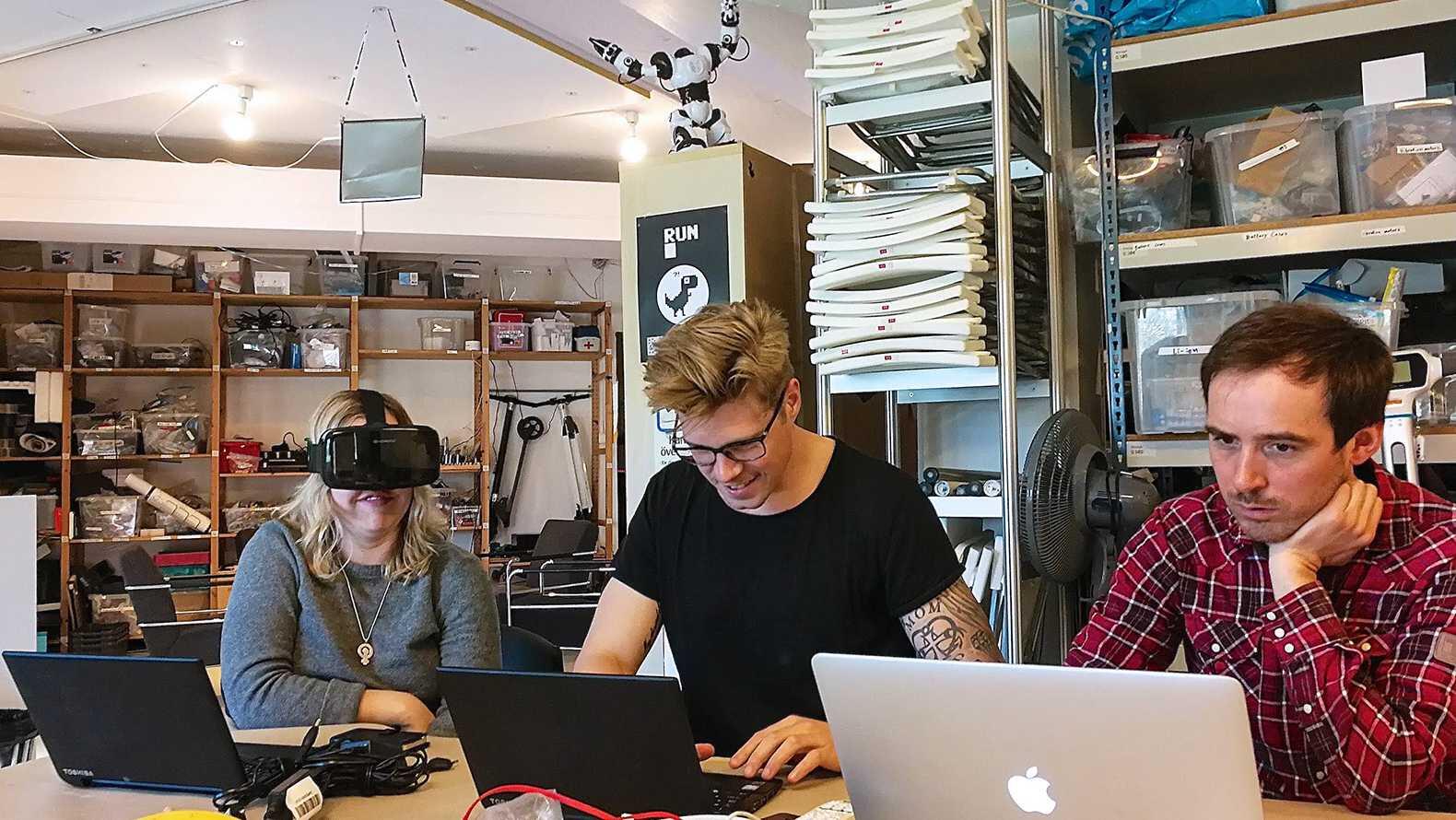 Personer vid skrivbord, skrattar, en har ett VRheadset på sig. 