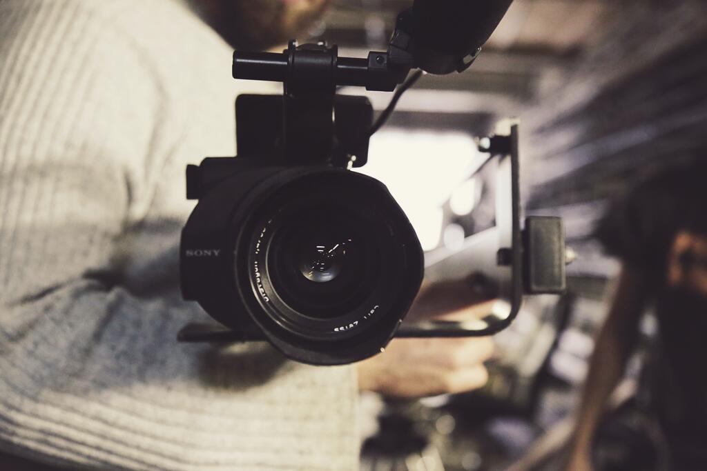 Närbild på en videokamera som hålls av en man i en vit stickad tröja 